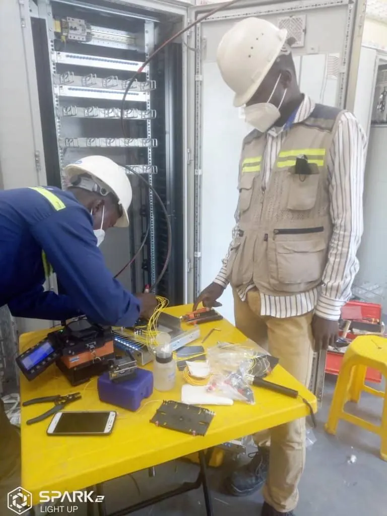 Two SPA technicians splicing fibre at a site cabinet, working from an open splicing kit