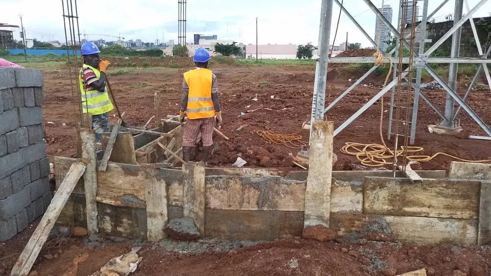 Crew casting reinforced tower foundations beside a part-erected lattice mast